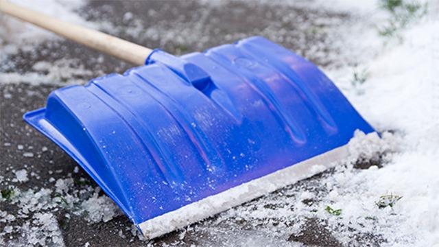 Blå sneskovl ligger på jorden med sne omkring, klar til at rydde sne fra fortovet.