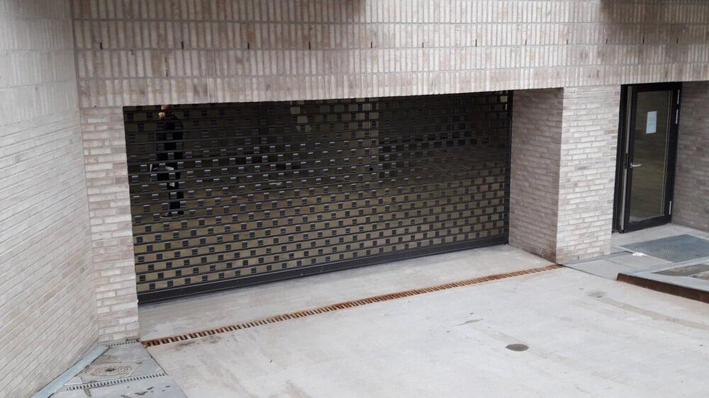 Lukket garageport med gitter foran en bygning, omgivet af mursten og beton.