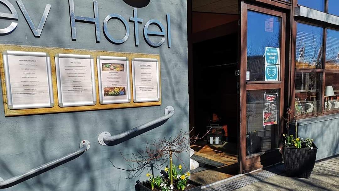 Indgangen til Rev Hotel med menuskilt og blomsterkasser ved døren.