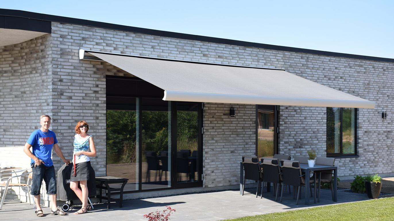 Moderne hus med terrasse, markise og to personer, der står ved siden af et udendørs spiseområde.
