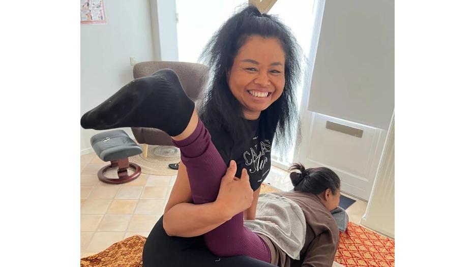 To kvinder, den ene smilende og i en yoga-position, mens den anden ligger på gulvet i stuen.