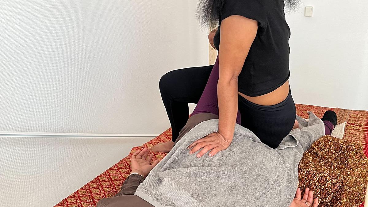 En person får massage, mens en anden person sidder på ryggen og anvender tryk på en rød måtte.