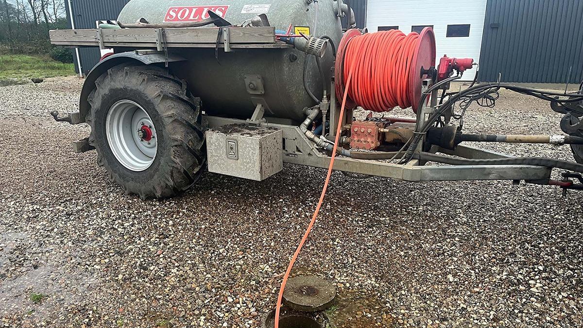 En gyllevogn med rød slange står på grus, klar til at blive brugt til gødning af marker.