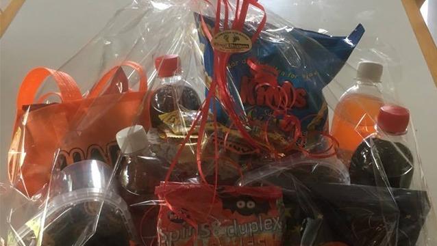 Gavekurv med sodavand, snacks og slik i orange emballage, præsenteret i en gennemsigtig plastikpose.