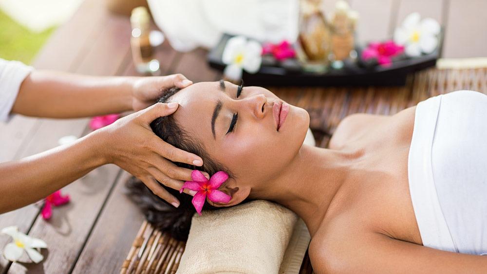 En kvinde får en afslappende hovedbundsmassage med blomster i håret i et spa-miljø.