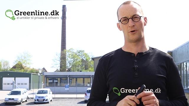 Mand står foran en bygning med en skorsten, mens han præsenterer Greenline.dk. Solrigt vejr.