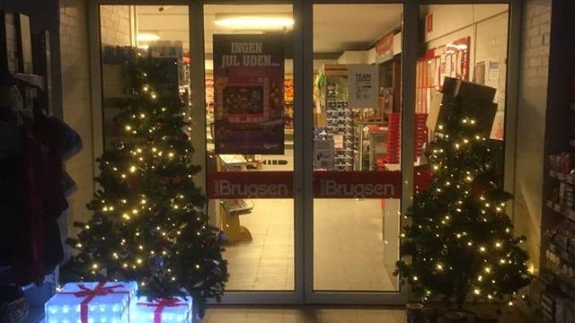Indgangen til en butik pyntet med juletræer og lys, samt gaver foran døren.
