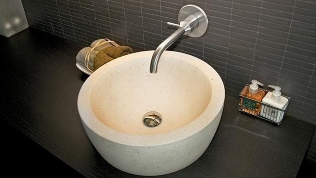 Vaskeskål i moderne design af lys sten med kromarmatur og sæbeprodukter ved siden af.