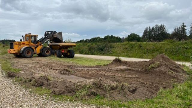 En gule gravemaskine arbejder på en grusvej, mens den flytter jord og skaber en ny overflade.
