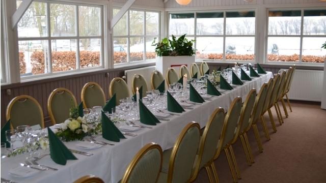 Et elegant dækket bord med grønne servietter i en lys restaurant med vinduer og udsigt til naturen.