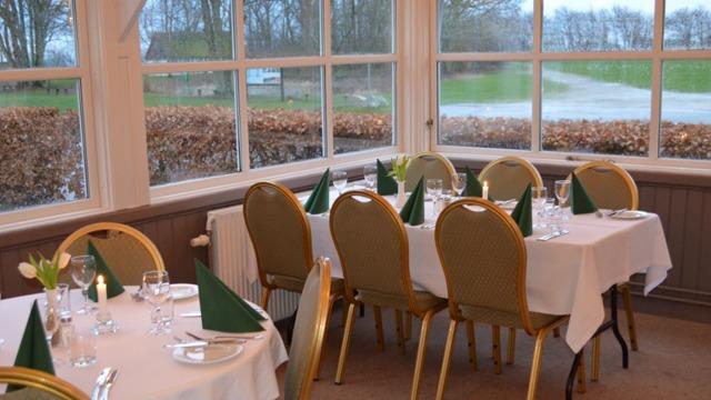 En elegant restaurant med dækkede borde, grønne servietter og udsigt til naturen gennem vinduerne.