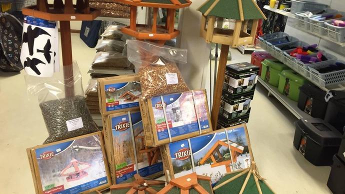 Fuglefodringsudstyr og fuglehuse i en butik, herunder foderautomater og tilbehør til fugle.