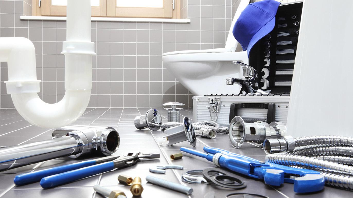 Værktøj og rørdele spredt ud på badeværelset ved siden af en toilet og en åben værktøjskasse.