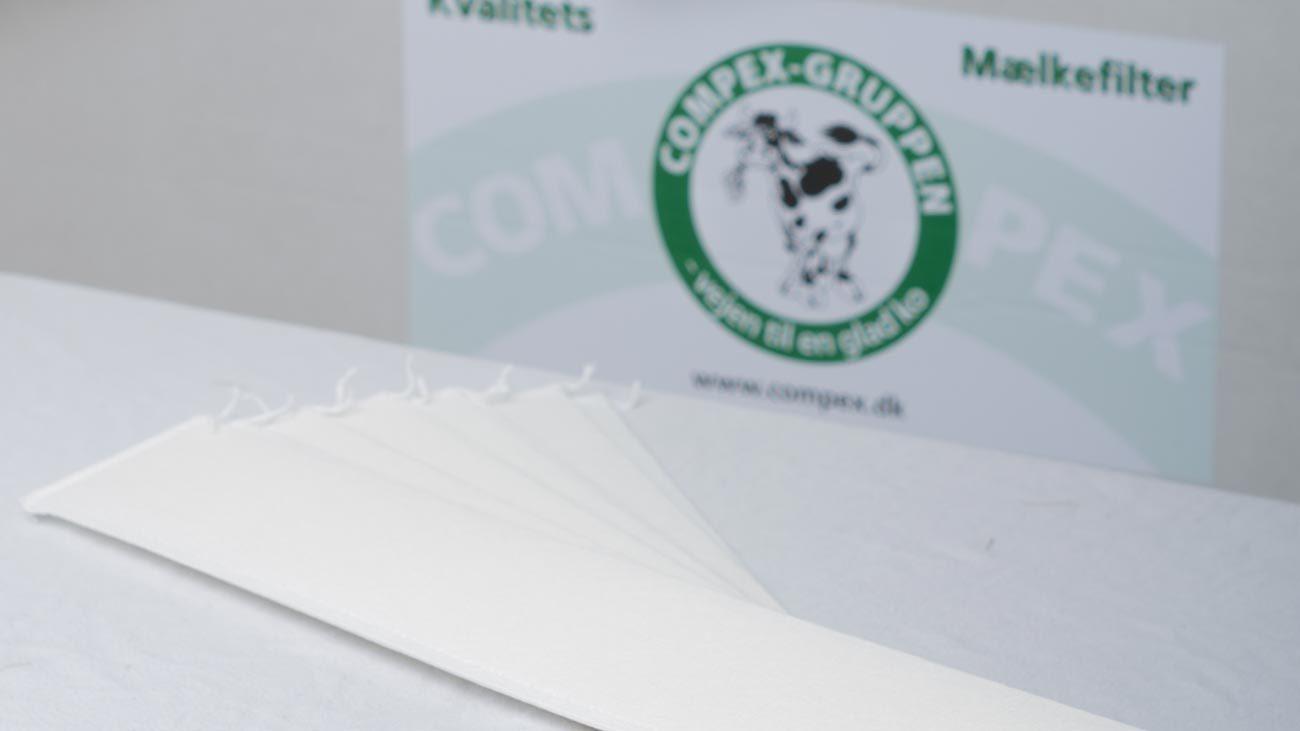 Hvidt malfilter til mælkeproduktion placeret på et bord med Compex-gruppens logo i baggrunden.