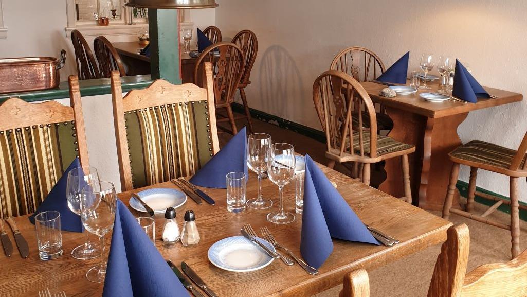 Indretning af en restaurant med træmøbler, blå servietter og dækkede borde klar til gæster.