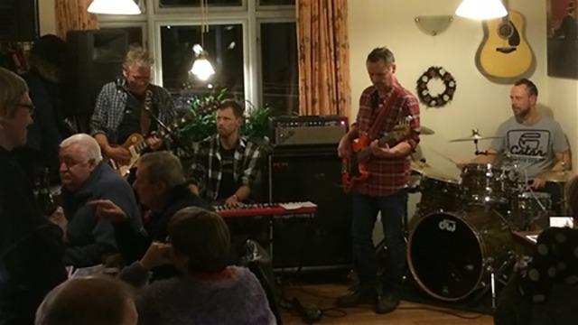 Et band spiller live musik i en hyggelig café, mens gæsterne nyder deres aften.