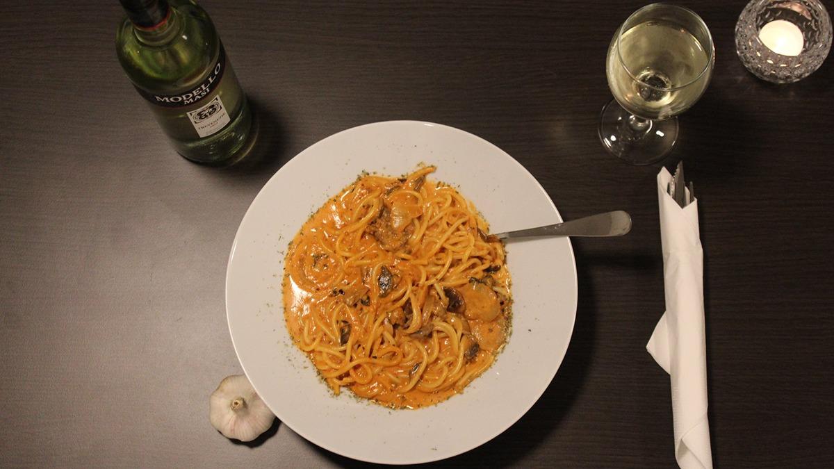 En tallerken med pasta i cremet sauce, rejer og muslinger, serveret med et glas hvidvin og en hvidløgsklove.