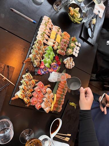 En stor sushi-anretning med forskellige typer sushi, grøntsager og saucer på et sort bord.