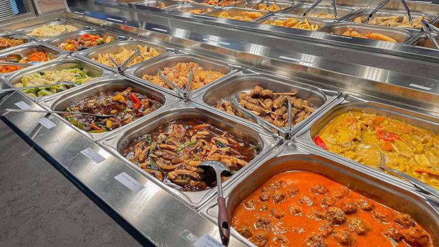 Et udvalg af varme retter i en buffet med forskellige grøntsager, kød og saucer.