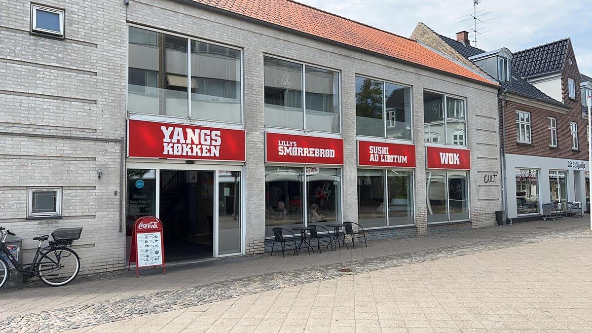 En bygning med tre butikker, herunder Yangs Kokken, Hjemmeservice og VIT, beliggende i en bygade.