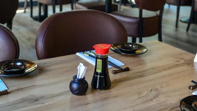 Et restaurantbord med brune stole, soyasauce, servietter og sorte skåle.