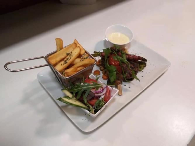 En tallerken med pomfritter i en kurv, salat, kød og en skål med sauce.