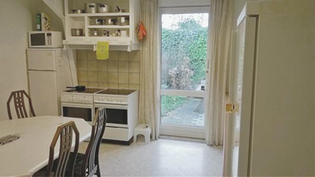 Køkken med hvidt skab, komfur, bord med stole og udsigt til en have gennem en glasdør.