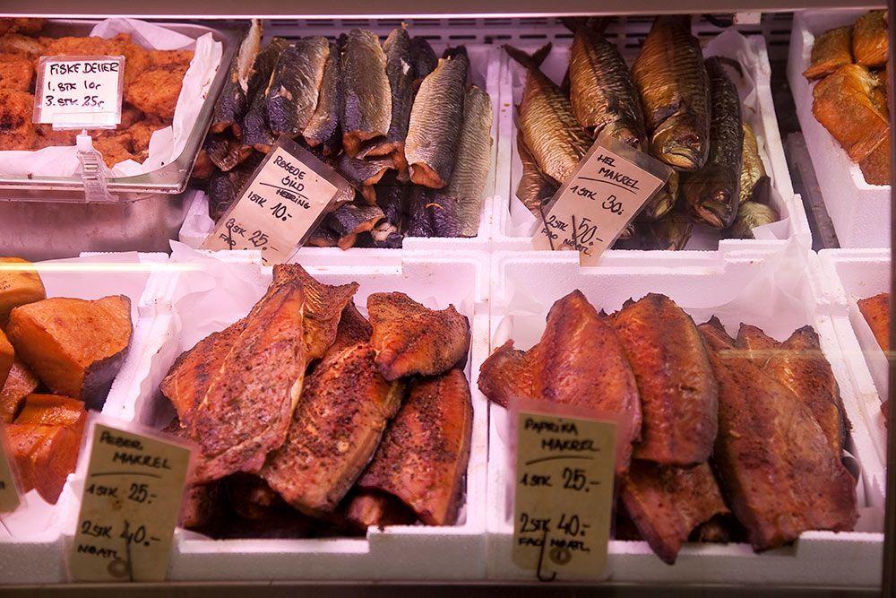 Fiskebutik med forskellige typer røget fisk, herunder makrel og laks, prissat og pakket i hvide kasser.