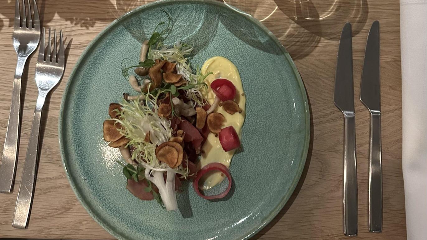 En farverig tallerken med salat, sprøde grøntsager og en cremet dressing, serveret med bestik på et træbord.
