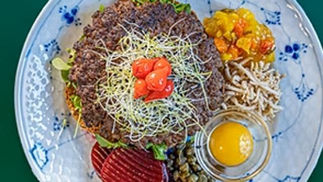 En tallerken med hakket oksekød, salat, cherrytomater, syltede grøntsager, kapers og et råt æg.