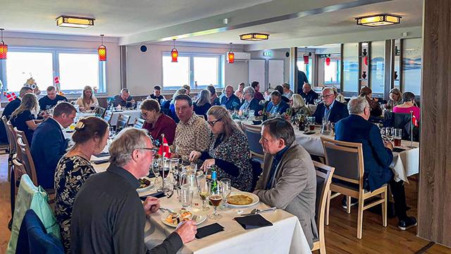 En livlig restaurant med gæster, der nyder middag ved borde, omgivet af vinduer og festlig indretning.