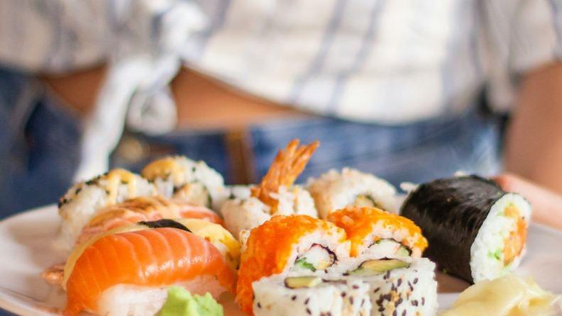 En tallerken med forskellige sushi-ruller, herunder laks, rejer og avocado, serveret med wasabi og ingefær.