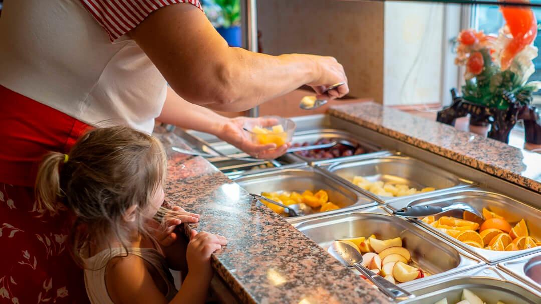 En voksen og et barn vælger frugt fra en buffet med forskellige frugter i skåle.