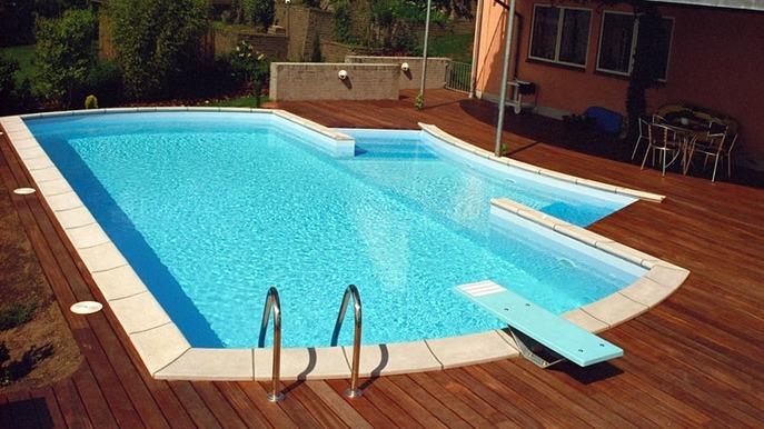 En swimmingpool med en dykkerbræt og træterrasse i en solrig have.