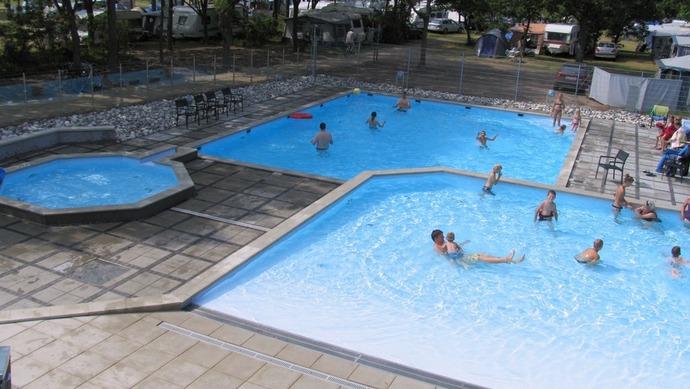 Børn og voksne svømmer i en stor swimmingpool med flere bassiner og solrige områder.