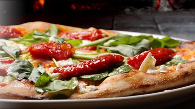 Lækker pizza med tomatsauce, friske spinatblade og soltørrede tomater på en hvid tallerken.