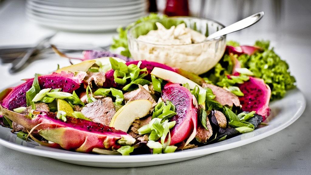 Farverig salat med grøntsager, æbler og en skål med dressing på en hvid tallerken.