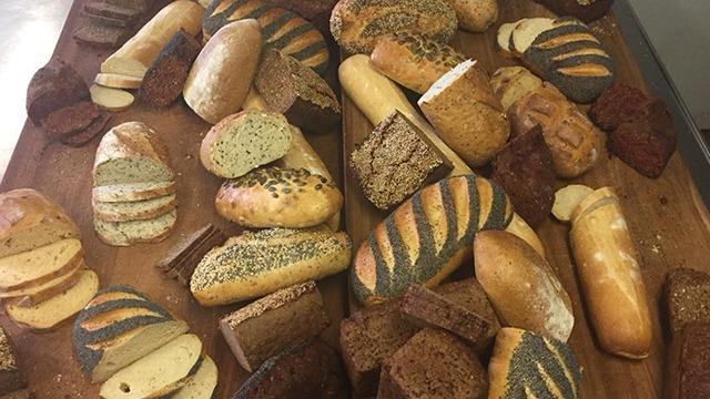 Forskellige typer brød og boller præsenteret på et træbord, herunder rugbrød og hvedebrød.