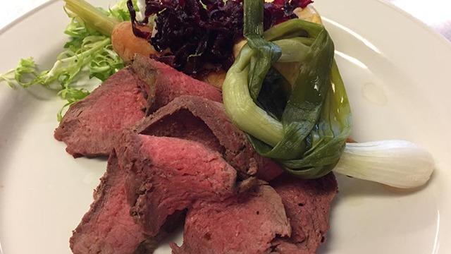 Mørt oksekød serveret med friske grøntsager og en farverig salat på en hvid tallerken.