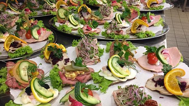 Forskellige anretninger med smørrebrød, grøntsager, urter og citrusfrugter på fade.