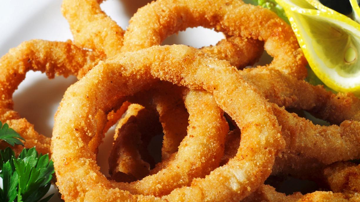 Sprøde, gyldne løgringe serveret med citron og friske krydderurter på en hvid tallerken.