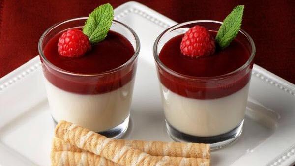 To små glas med dessert, toppet med hindbær og mynte, serveret med vafler på en hvid tallerken.