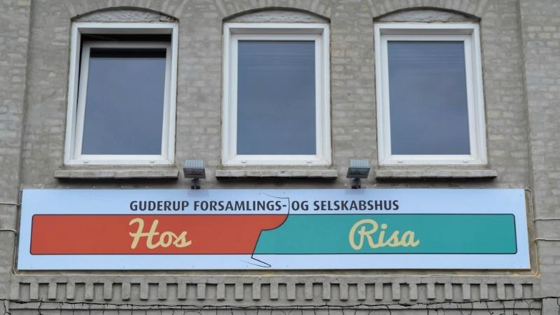 Guderup forsamlings- og selskabshus med skiltet "Hos Risa" på væggen.