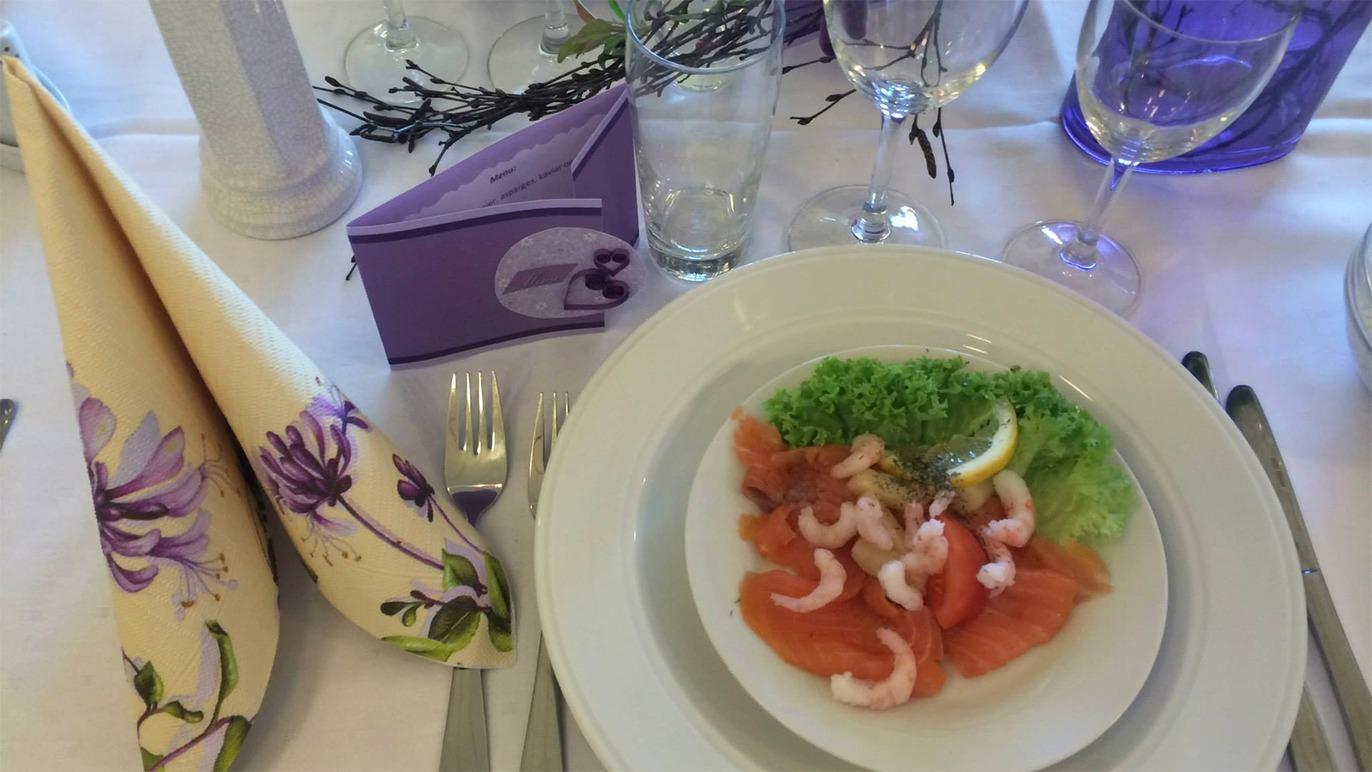 En elegant anretning med røget laks, rejer, salat og citron på en hvid tallerken, omgivet af smukt borddækning.