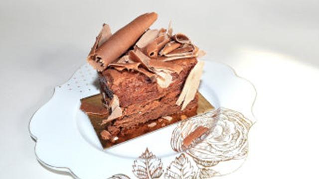 En lækker chokoladekage med chokoladeflager og kanelstænger på en hvid tallerken.