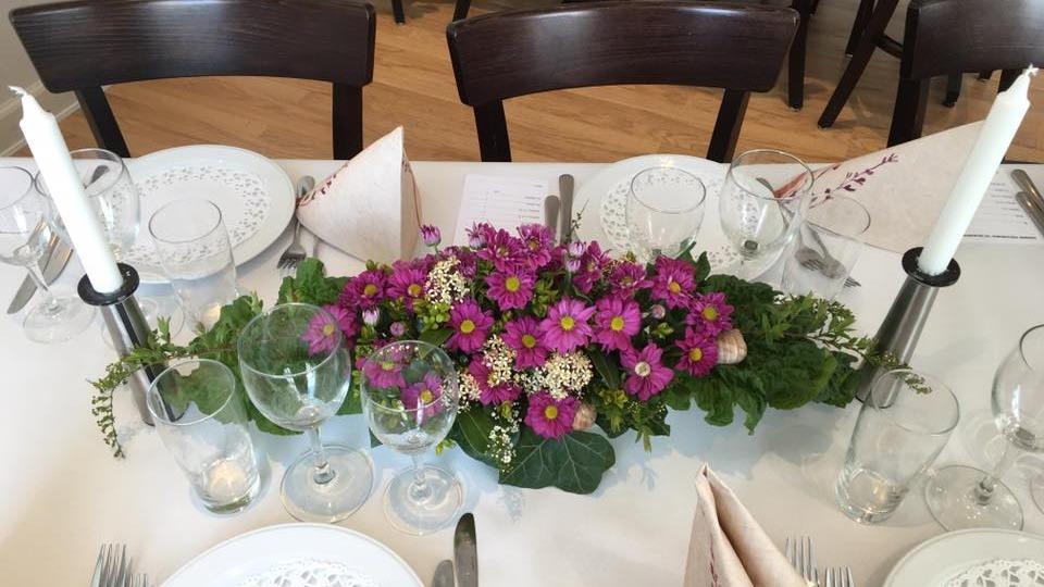 Smukt dækket bord med blomsterdekoration, glas og stearinlys til festlig lejlighed.