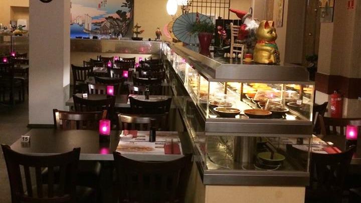 Indendørs restaurant med borde, stole og en buffet med mad, oplyst af lilla lys.