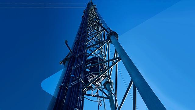 Et højt mobilmaster med antenner mod en klar blå himmel.