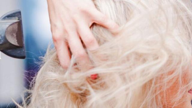 Hånd, der griber fat i lyst hår, mens en hårtørrer bruges til at style frisuren.