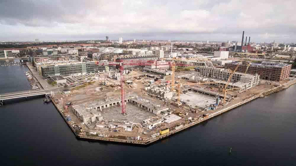 Luftfoto af en byggeplads ved havnen med kraner og bygninger under opførelse.